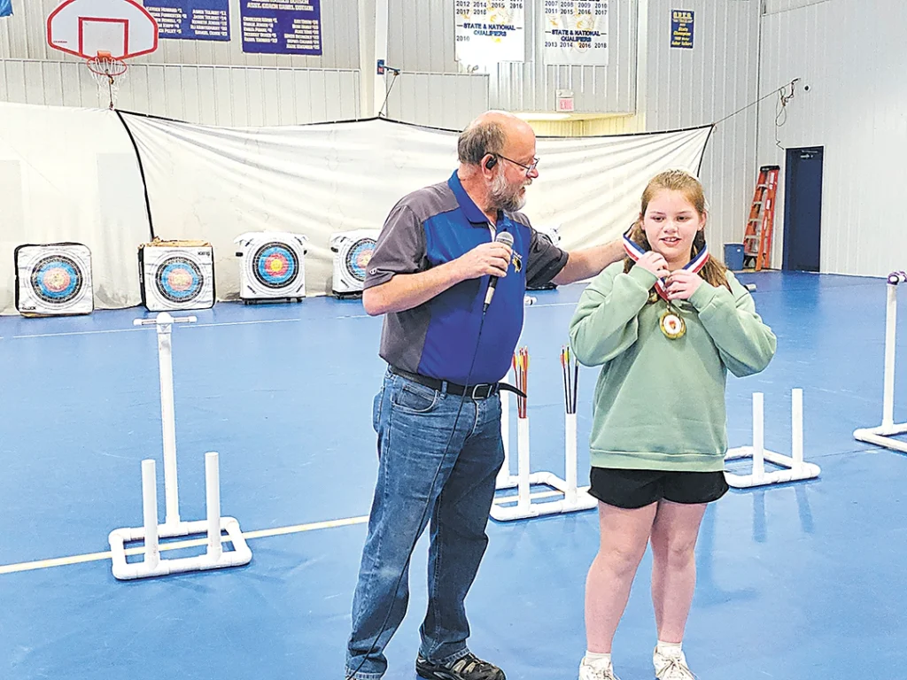 CHARLES BETZLER PHOTO ANNISTON BOWLING OF PRETTY WATER SCHOOL (right) is presented with the 5th-Grade girls archery state championship medal by her archery instructor, Robert Gaches, on Friday