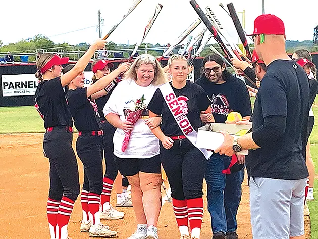 UNDER THE BATS Senior catcher Lil Bacon (center) walks under the bats with her mom Leann and dad Craig.