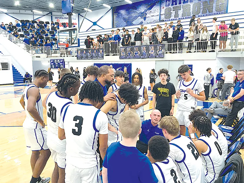 JOHN TRANCHINA PHOTOS SAPULPA COACH JORDAN NAGEL (center, squatting) talks to his team after the first quarter Tuesday night, with a large student section and the Sapulpa band (upper left) watching.