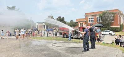 CHARLES BETZLER PHOTOS SAPULPA FIREFIGHTER TAYLOR LEWIS mans the fire hose as the children frolic in the water across the street from the Library.